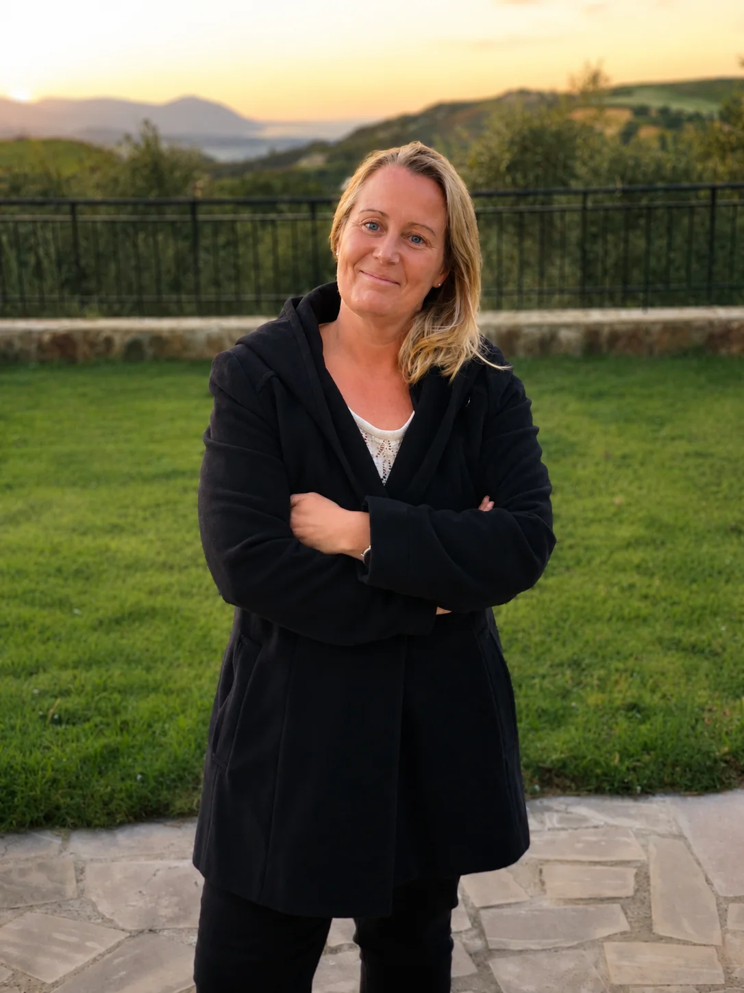 Stefanie Lenzen steht abends im Garten, hinter ihr Wiesen und Hügel im Abendlicht